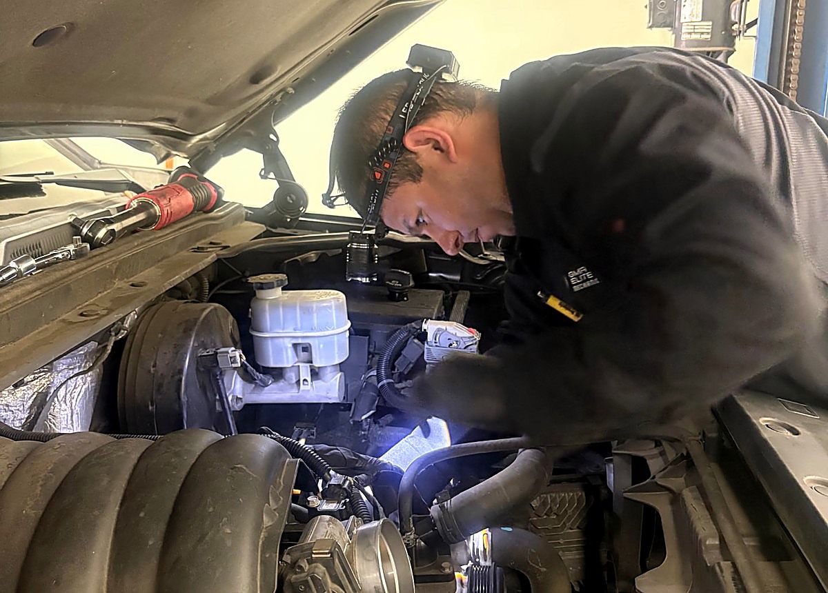 GMR technician with a headlamp working in an open engine bay at the shop