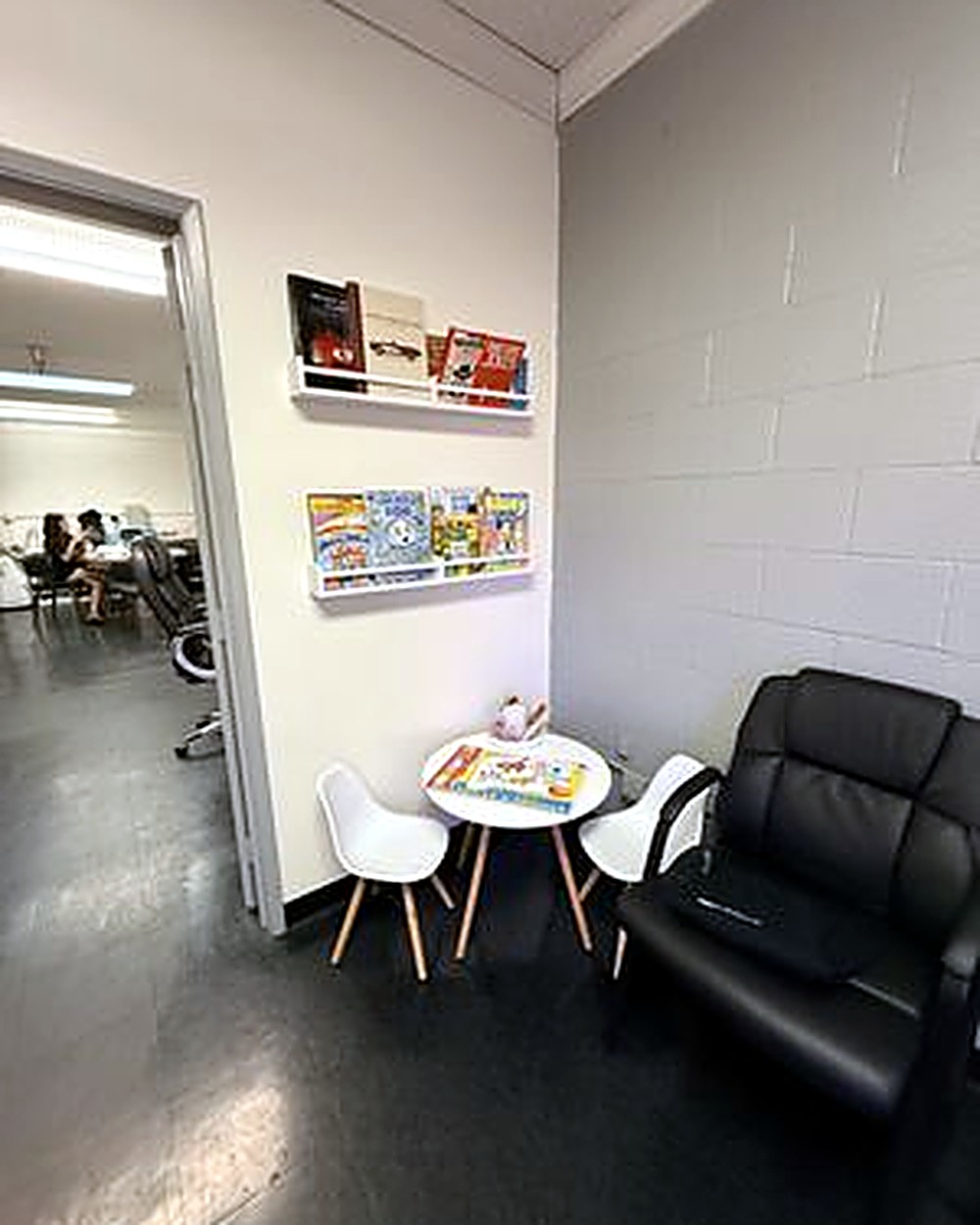 Waiting area corner with children's books on floating shelves, a small table and chairs, and a waiting chair